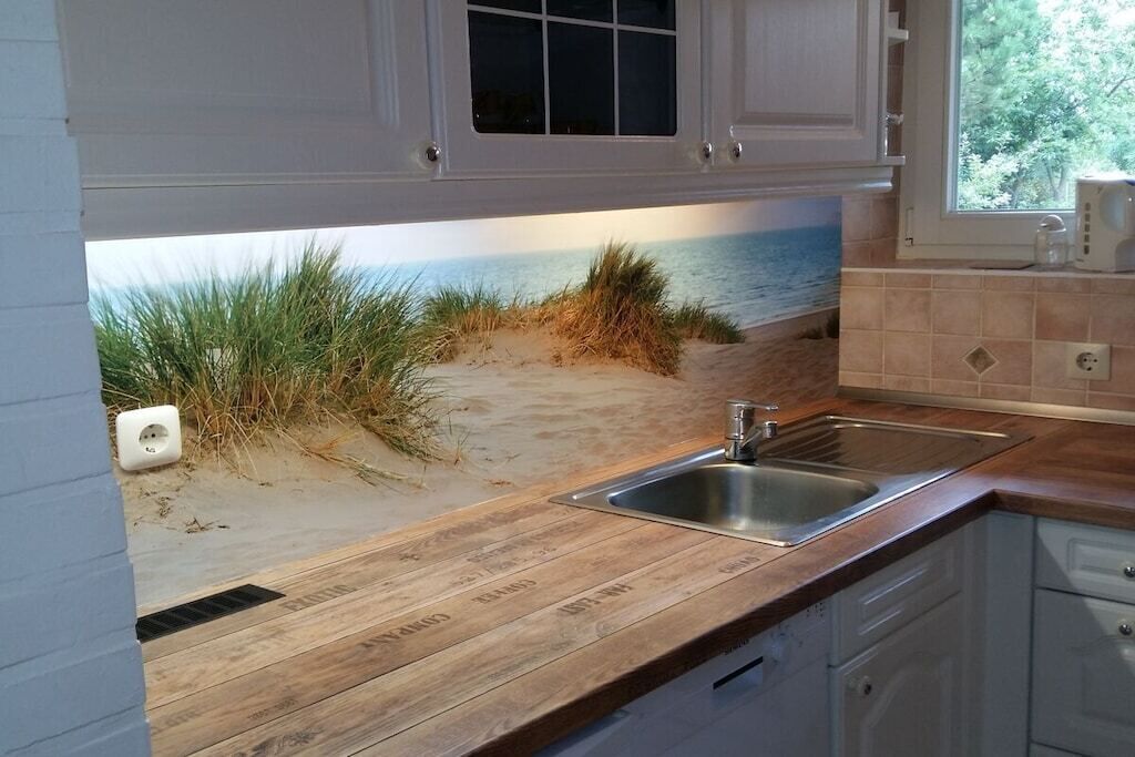 A kitchen with a wooden countertop, a stainless steel sink, and a window with a view of the beach.