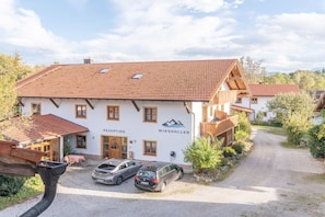 A two-story building with a reception area, a parking lot with cars, and a gravel driveway. - Apartment 16 with lake view (Chieming)