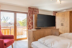 A bedroom with a bed, a television on a wooden stand, a red chair, and a sliding glass door leading to a balcony. - Apartment 16 with lake view (Chieming)