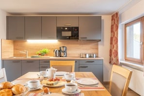A modern kitchen with grey cabinets, a wooden countertop, and a dining area with a table set for breakfast. - Apartment 16 with lake view (Chieming)
