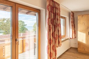 A room with a wooden door, a window with curtains, and a view of the outdoors. - Apartment 16 with lake view (Chieming)