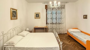 A bedroom with a large bed, a smaller bed, a desk, a chair, a nightstand, and a window with curtains.
