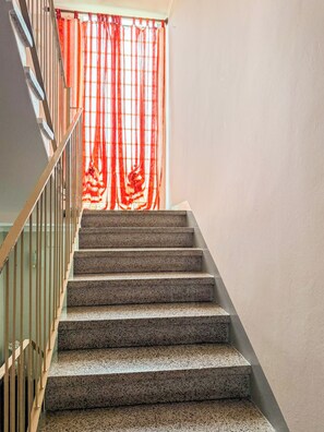 A staircase with a handrail and a view of a room through a window with red curtains. - A5minutidallagodorta (Gozzano)