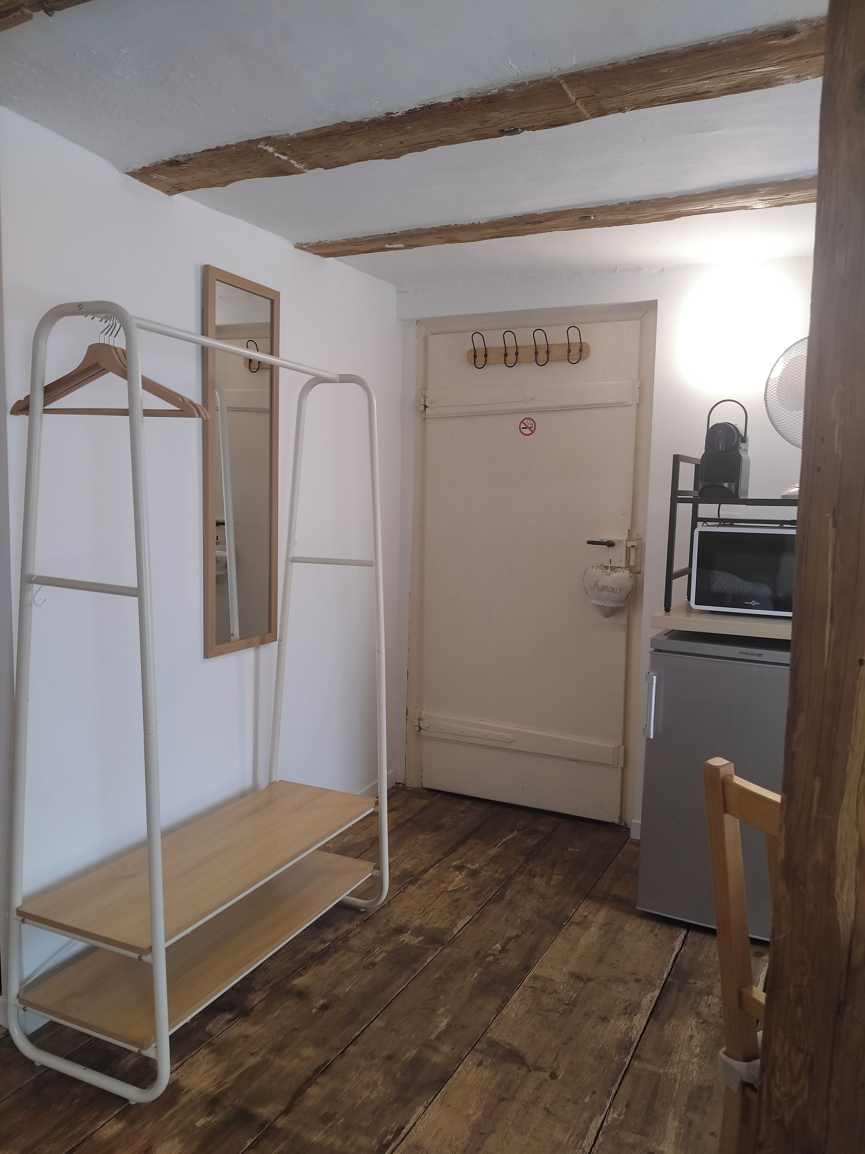 Une pièce avec un plancher en bois, une porte blanche portant un panneau «interdiction de fumer», une étagère en métal, une chaise en bois et un petit réfrigérateur.