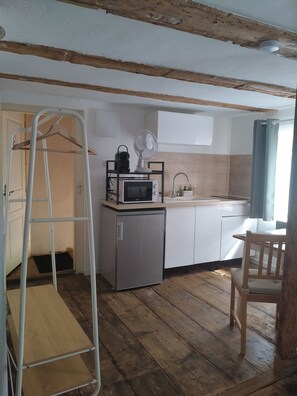 Eine kleine Küche mit Holzboden, einem Kühlschrank, einer Mikrowelle, einem Ventilator und einem Holzstuhl.