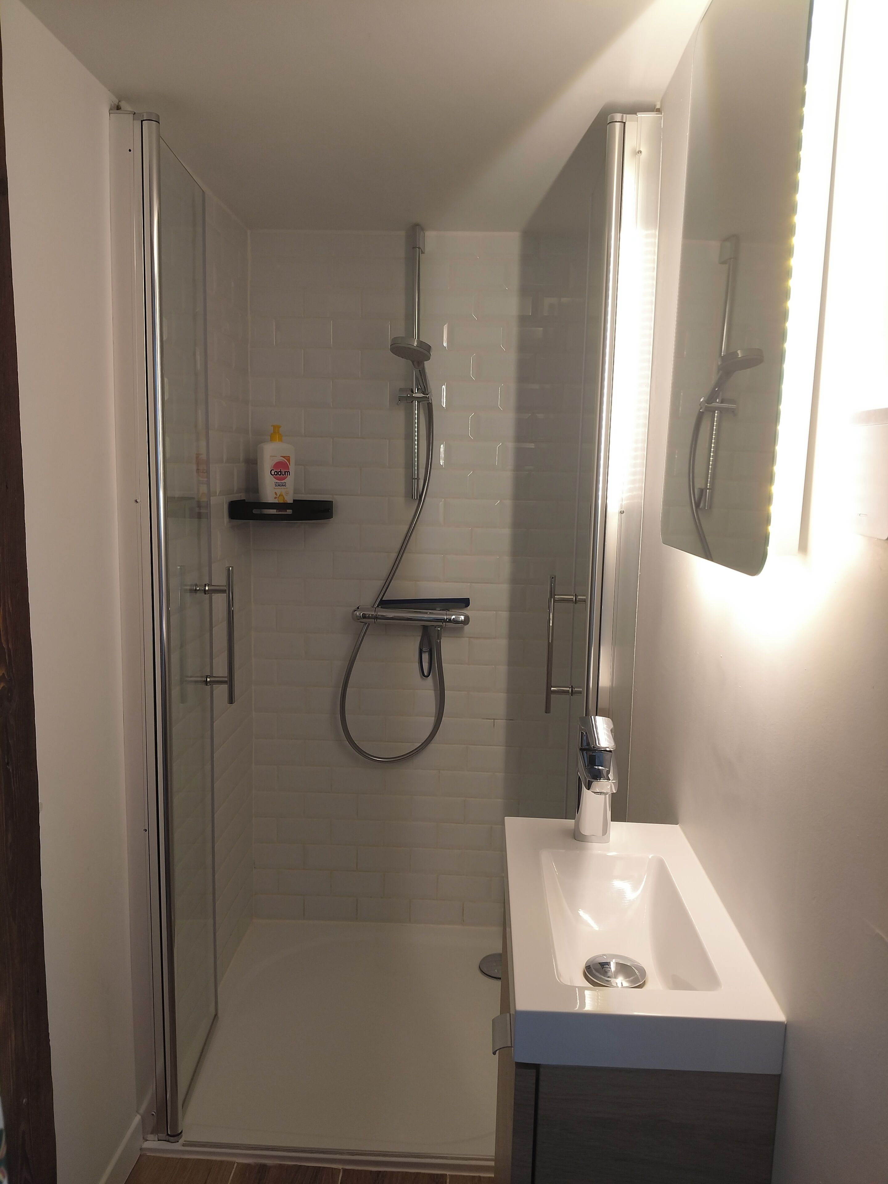 Ein modernes Badezimmer mit einer gläsernen Duschkabine, einem weißen Waschbecken und einem Spiegel mit integrierter Beleuchtung.
