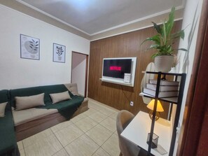 A living room with a sofa, a TV mounted on a wooden wall, a small table with a lamp, and a potted plant. - Vrbo Property (Franca)