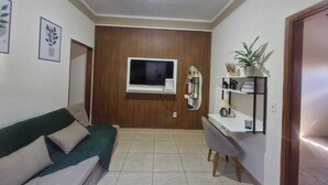 A living room with a sofa, a TV, a mirror, and a shelf with decorative items.