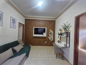 A living room with a sofa, a TV, a mirror, and a shelf with decorative items.