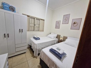 A hotel room with two beds, a wardrobe, a window with blinds, and a wall with framed artwork. - Vrbo Property (Franca)
