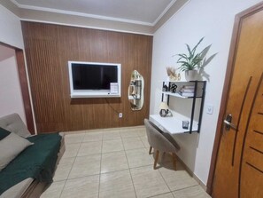 A room with a bed, a TV mounted on the wall, a mirror, a shelf with decorative items, and a door.