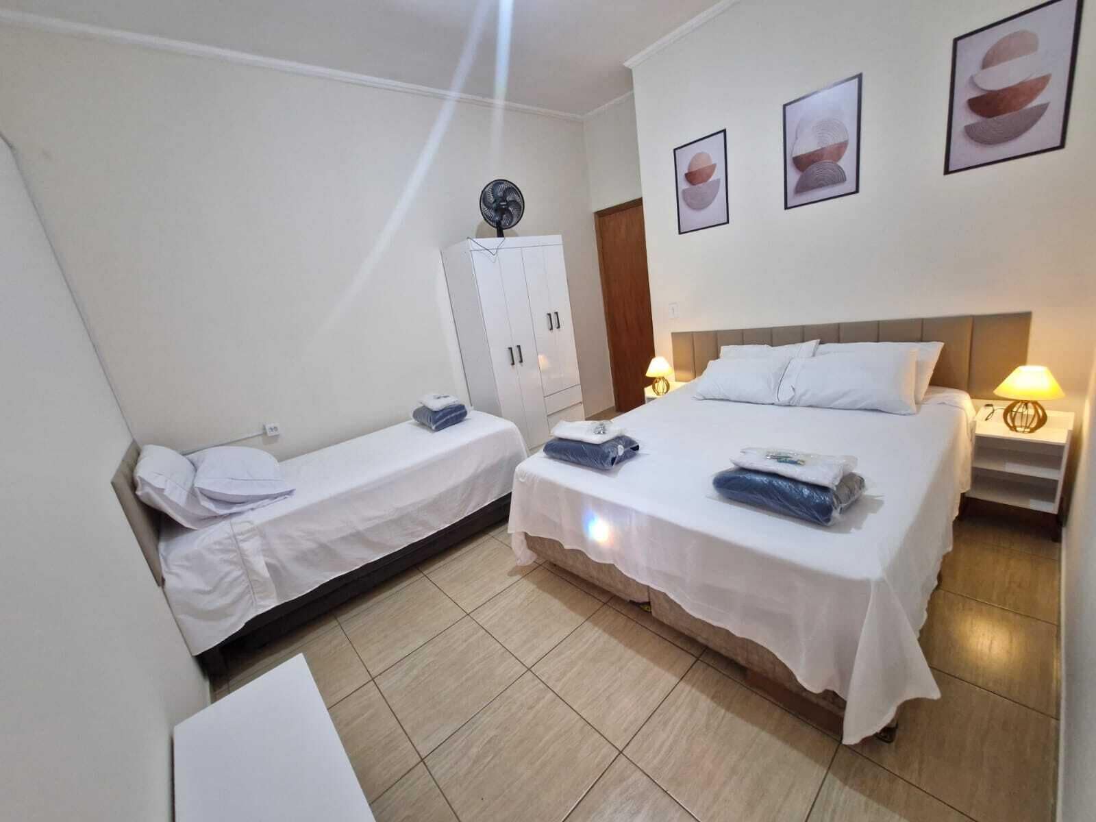 Habitació d'hotel amb dos llits individuals, un armari, una taula de nit amb una làmpada i una obra d'art a la paret.