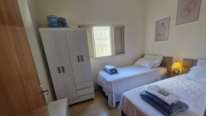 A room with two beds, a wardrobe, a window with blinds, and a wall with a framed picture.