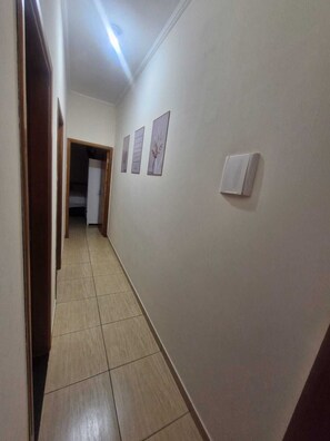 A hallway with a tiled floor, a door on the left, and three framed pictures on the wall.
