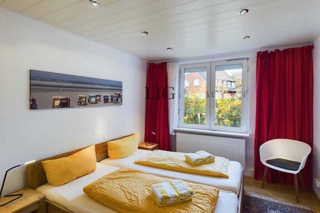 Een hotelkamer met twee bedden, een raam met rode gordijnen, een stoel en een spiegel aan de muur.
