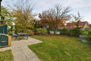 A residential backyard with a patio table and chairs, a wooden deck, and a lawn. - Holiday apartment Palladium 4 (Langeoog)