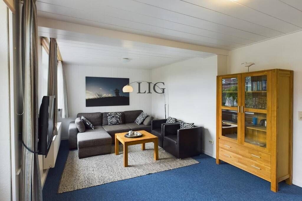 A modern living room with a sectional sofa, a coffee table, a cabinet with glass doors, and a wall-mounted artwork.