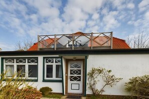 A house with a white exterior, green trim, a red-tiled roof, and a balcony with a railing. - Holiday apartment Palladium 4 (Langeoog)