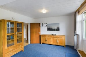 A room with a blue carpet, a wooden cabinet, a wooden door, and a wall-mounted picture. - Holiday apartment Palladium 4 (Langeoog)