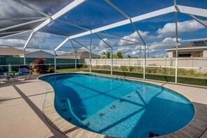 A swimming pool with a covered area, surrounded by a fence and palm trees. - Holiday home with 1 bedroom (Cape Coral)