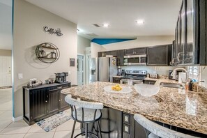 A modern kitchen with granite countertops, dark cabinetry, and a central island with bar stools. - Holiday home with 1 bedroom (Cape Coral)