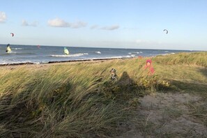A beach with windsurfing activity, grassy dunes, and a clear sky. - House by the farm garden, Michel holiday farm (Fehmarn)