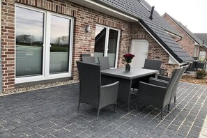 Een terras met een tafel en stoelen, een bakstenen muur en een schuifdeur.