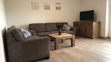 Ein Wohnzimmer mit braunem Sofa, einem Holztisch und einem Fernseher auf einer Holzkommode.