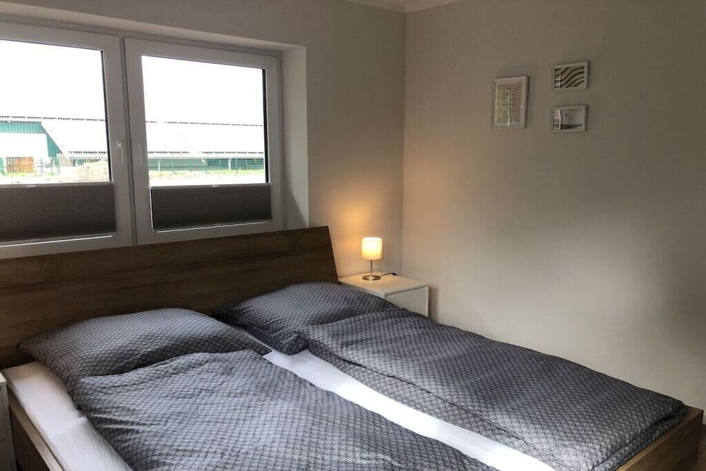 Ein Schlafzimmer mit einem Bett, einem Nachttisch mit Lampe, einem Fenster und einer Wand mit drei gerahmten Bildern.