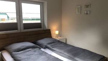 Ein Schlafzimmer mit einem Bett, einem Nachttisch mit Lampe, einem Fenster und einer Wand mit drei gerahmten Bildern.
