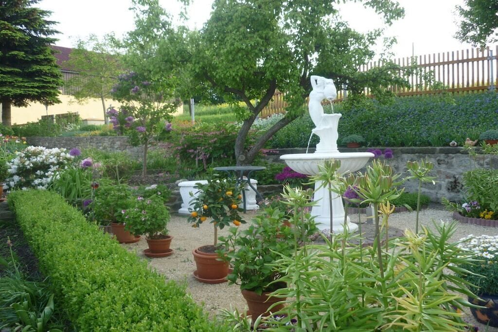 A garden with a white fountain, potted plants, and a variety of flowers.
