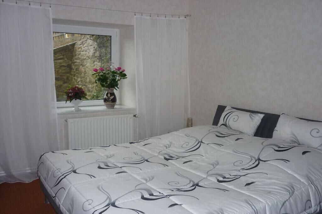 A bedroom with a bed, a window with curtains, and a view of a stone wall.