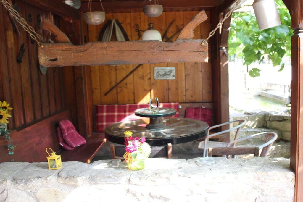 Un intérieur rustique en bois, avec une table en pierre, un banc et une cloche suspendue.