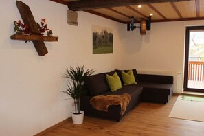 A living room with a dark brown sofa, a potted plant, and a wooden shelf with decorative items. - Holiday apartment with 1 bedroom (Oberstetten)