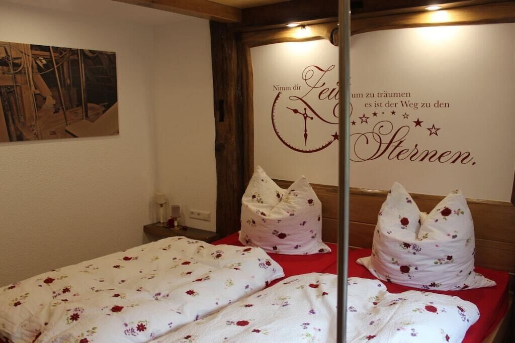 Une chambre d’hôtel avec un lit recouvert d’une literie à motifs floraux, un mur orné d’une inscription décorative et une tête de lit en bois.