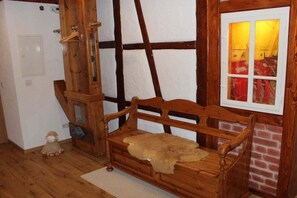 Un banc de fusta amb una manta de pell, un penjall de fusta i una porta blanca.