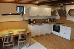 Eine Küche mit weißen Schränken, einem Holztisch, zwei Stühlen, einer hängenden Pflanze und einem eingebauten Backofen.