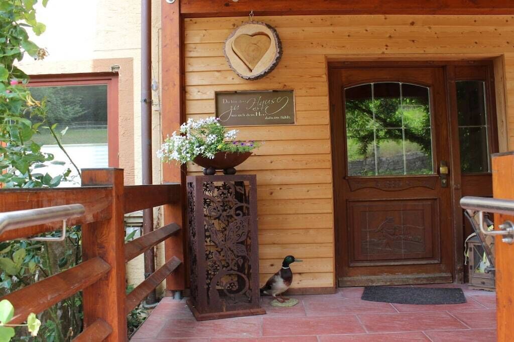 A wooden building entrance with a heart-shaped decoration, a sign, and a bird.