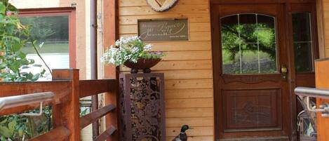 A wooden building entrance with a heart-shaped decoration, a sign, and a bird.