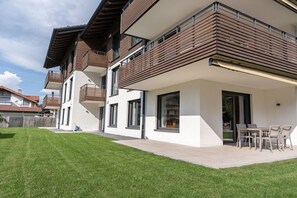 A modern two-story residential building with a balcony, a patio with outdoor furniture, and a well-maintained lawn. - Holiday apartment Villa Alpjuwel-Edelweiß (Oberstdorf)