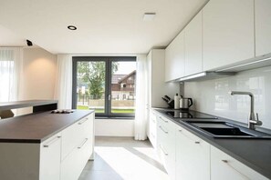 A modern kitchen with white cabinets, a black countertop, and a window providing a view of the outside. - Holiday apartment Villa Alpjuwel-Edelweiß (Oberstdorf)