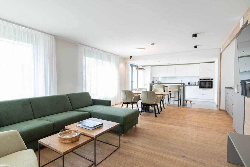 A modern living space with a green sofa, a wooden coffee table, and a dining area with chairs.
