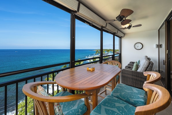 A balcony with a wooden table and chairs, a ceiling fan, and a view of the ocean. - Kona Alii#704: 7th Floor Penthouse, Direct Oceanfront, Remodeled & Ac (Kailua Kona)