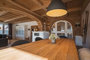 Un tavolo da pranzo in legno con un vaso di fiori, una lampada a sospensione moderna e un interno rustico con travi in legno e un armadietto bianco.