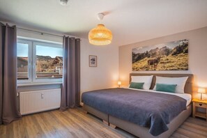 Una camera da letto con un letto grande, una finestra con tende, un quadro appeso al muro e una lampada a soffitto.