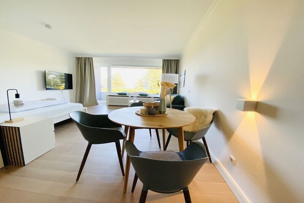 Ein modernes Wohnzimmer mit einer Couch, einem Esstisch mit Stühlen, einem flachbildfernseher an der Wand und einem Fenster mit Vorhängen.