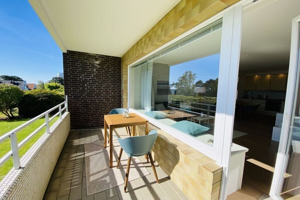 Un balcone con tavolo e sedie, una porta vetrata che dà su un ambiente interno e vista sull'esterno.