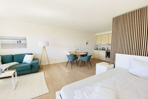 A hotel room with a bed, a sofa, a dining table with chairs, a small kitchen area, and a painting on the wall. - Holiday apartment with 1 bedroom (Travemünde)