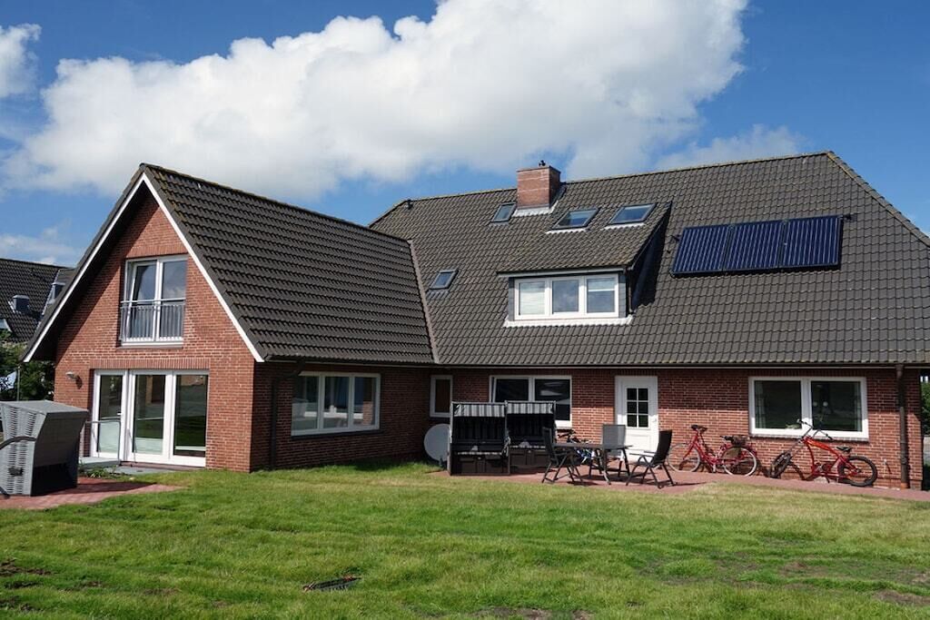 Ein zweistöckiges Haus mit einem geneigten Dach, Solaranlagen und einer Terrasse mit Gartenmöbeln.