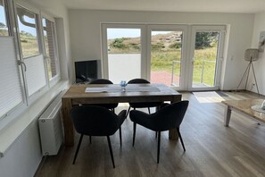 A room with a wooden table, two black chairs, a television, and a view through large glass doors to an outdoor area. - Apartment 2 in the Mare Cimbria building (Norddorf auf Amrum)